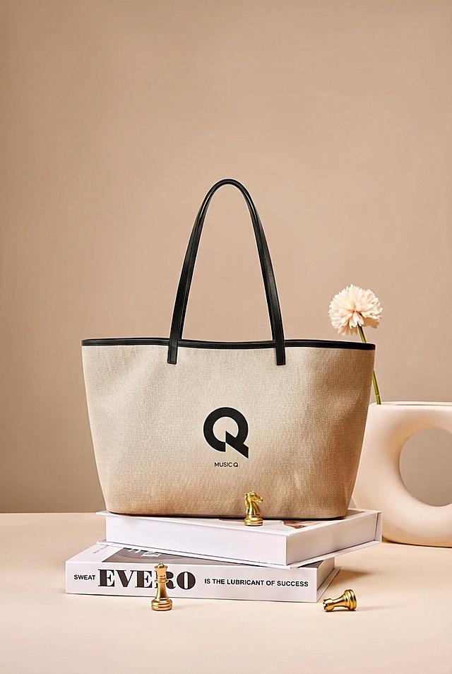 将米白色帆布托特包（带有黑色Q形logo和黑色包边、提手）自然融入奶咖色背景的桌面场景中，移除场景中原有的棕色包包，保留书籍、金色国际象棋棋子、白色异形花瓶和浅粉色花朵等道具。光影匹配场景的暖调柔和柔光，在包的底部生成自然的接触阴影，包身添加环境的暖棕色漫反射，消除边缘白边，调整包的摆放角度和位置与场景道具搭配协调，实现真实融合，整体为法式奶油风商业产品摄影质感，画面清晰细腻。